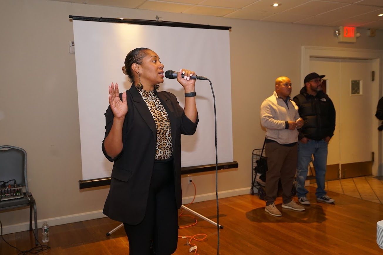 A woman is singing into a microphone in front of a projector screen.