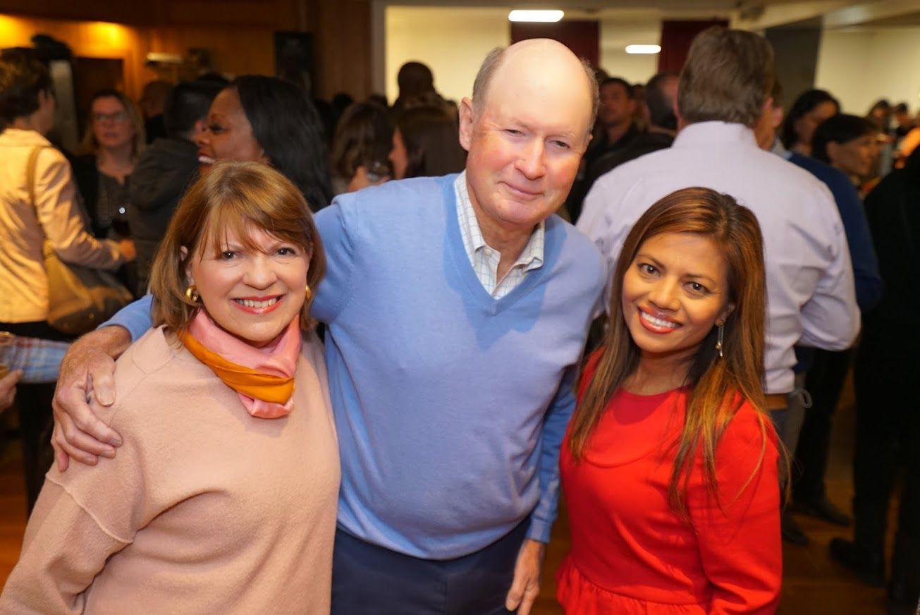 A man and two women are posing for a picture in a crowded room.