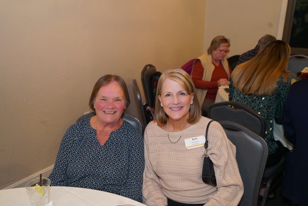 Two women are posing for a picture while sitting at a table.