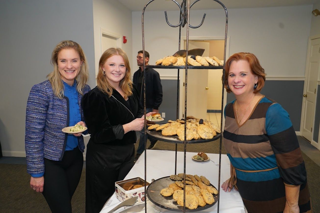 Three women are standing in front of a display of cookies.