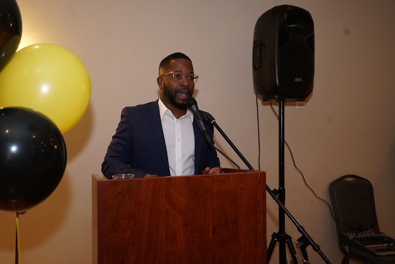 A man is standing at a podium speaking into a microphone.