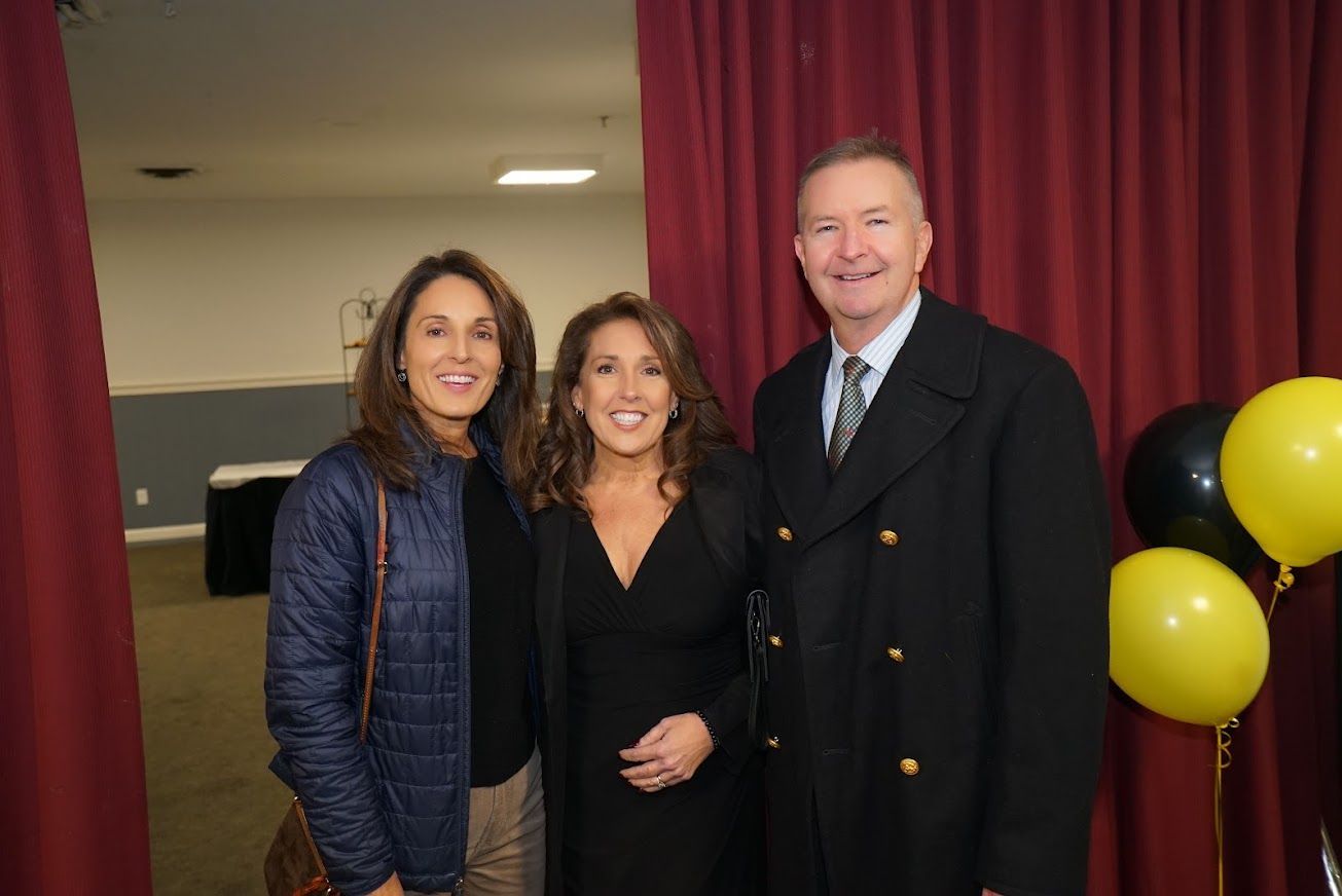 Three people are posing for a picture in front of a red curtain.