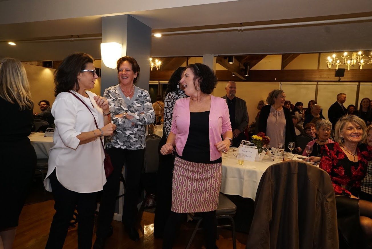 A group of women are dancing in a room with tables and chairs.