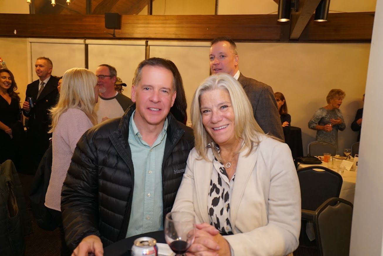 A man and a woman are sitting at a table with a glass of wine.