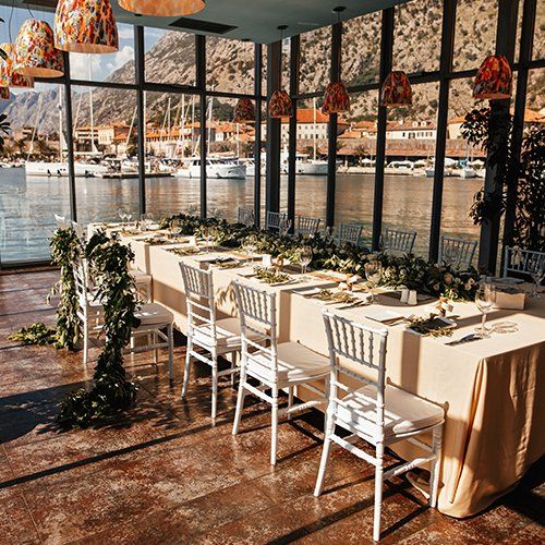 A long table and chairs in a room with a view of the water.