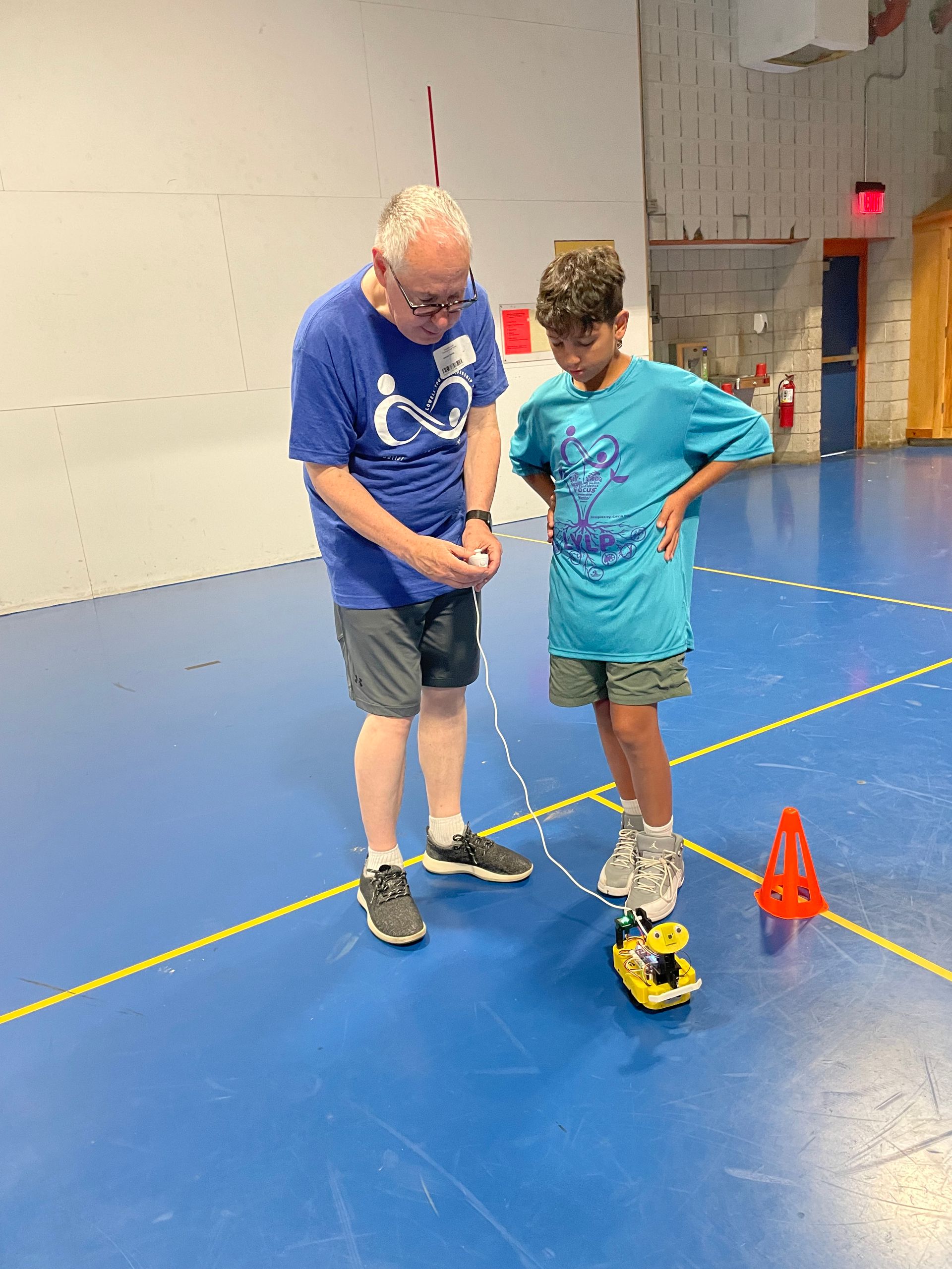 A man and a boy are playing with a toy car on a blue floor.