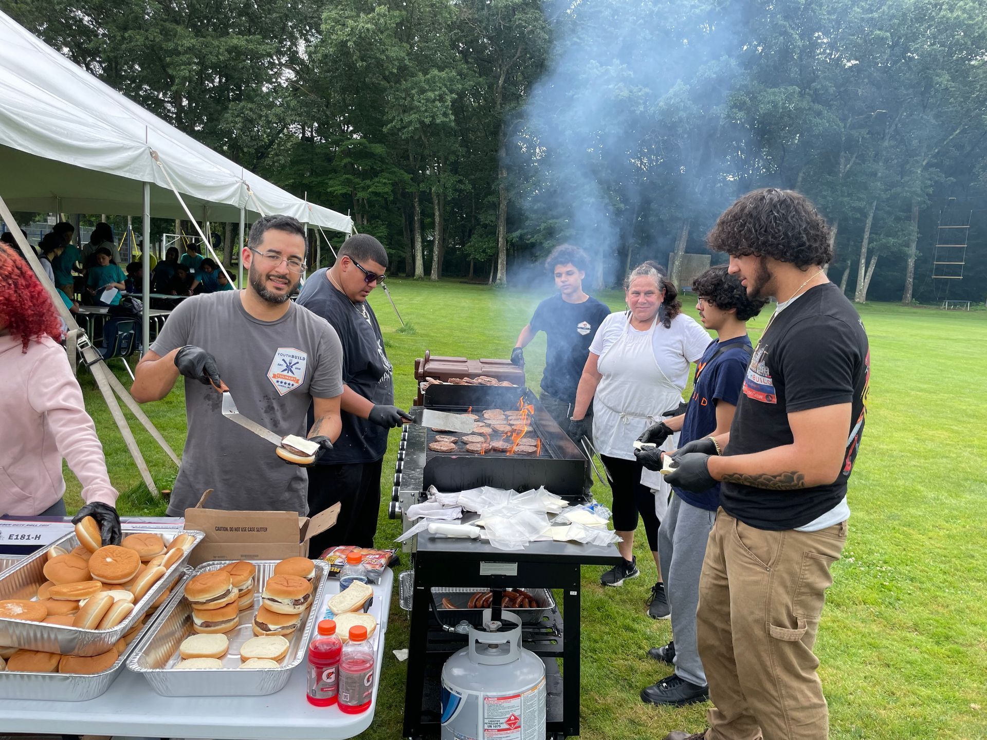 A group of people are standing around a table cooking food on a grill.