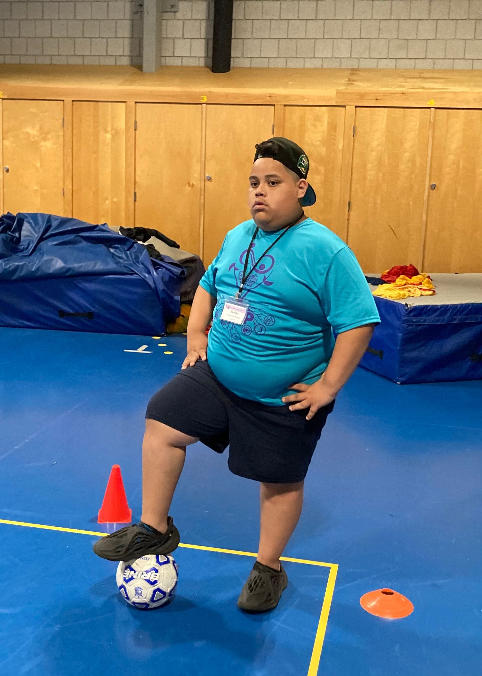 A boy in a blue shirt is standing on a soccer ball