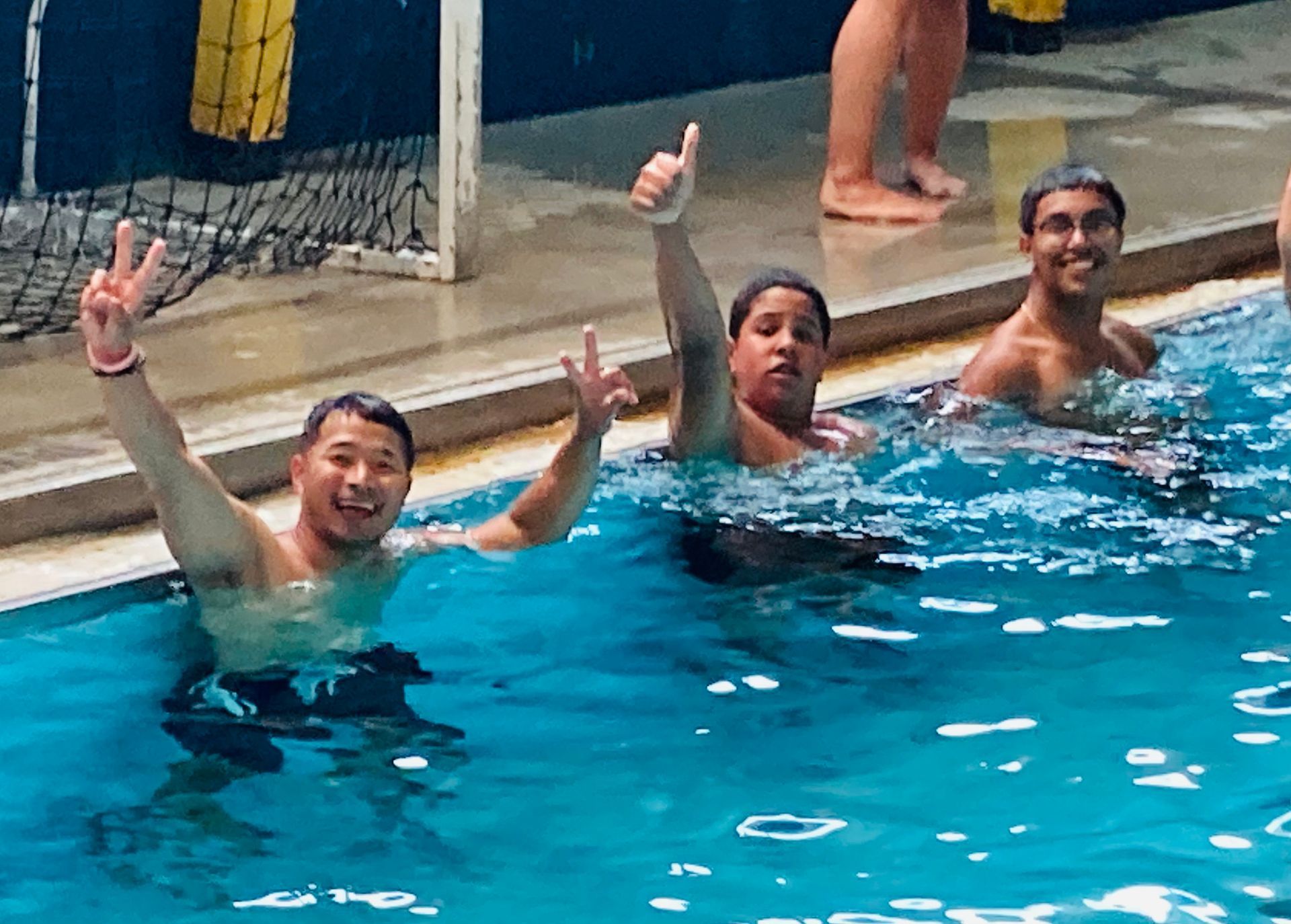 Three people are swimming in a pool and one of them is giving a peace sign.