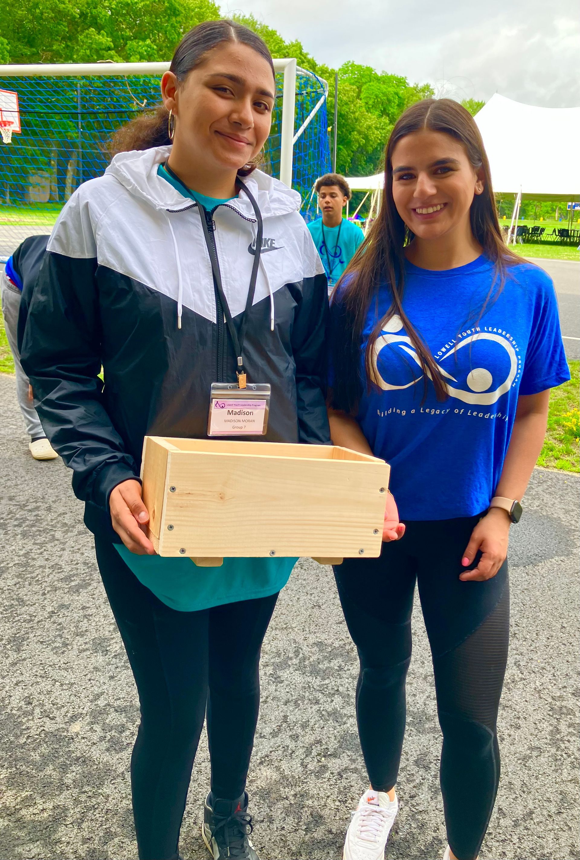 Two women are standing next to each other holding a wooden box.