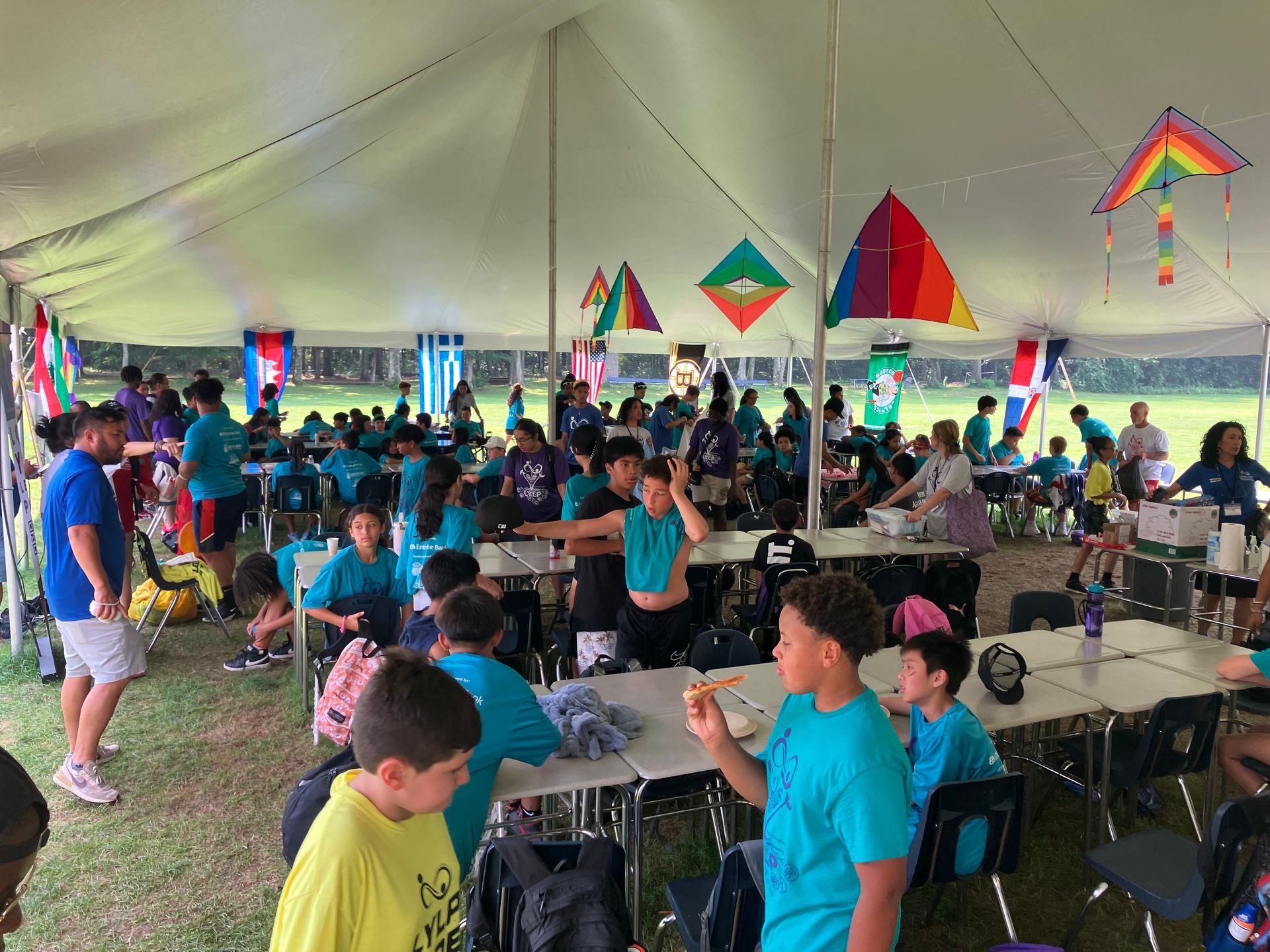 A group of children are sitting at tables under a tent.