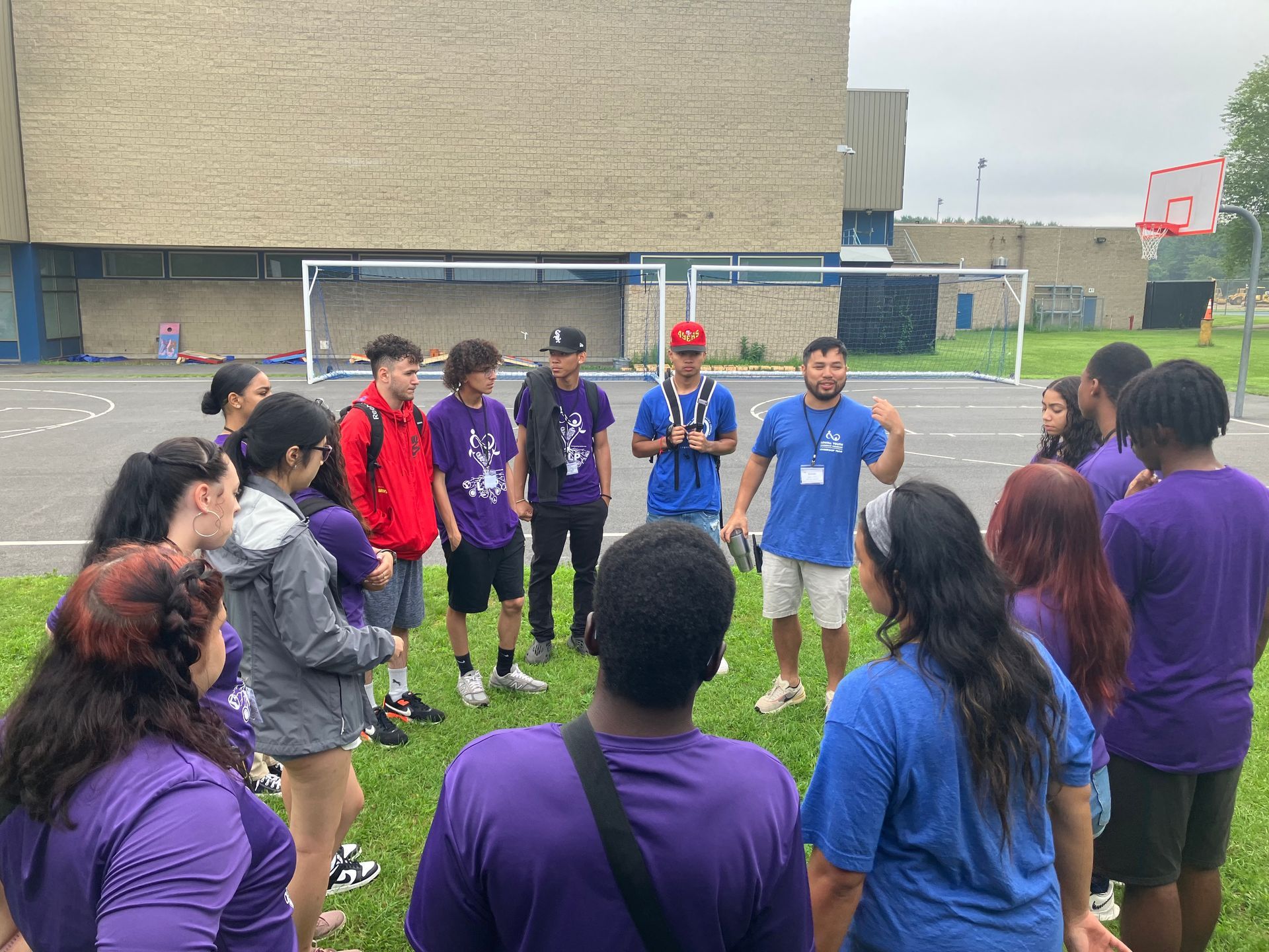 A group of people are standing in a circle in front of a basketball court.