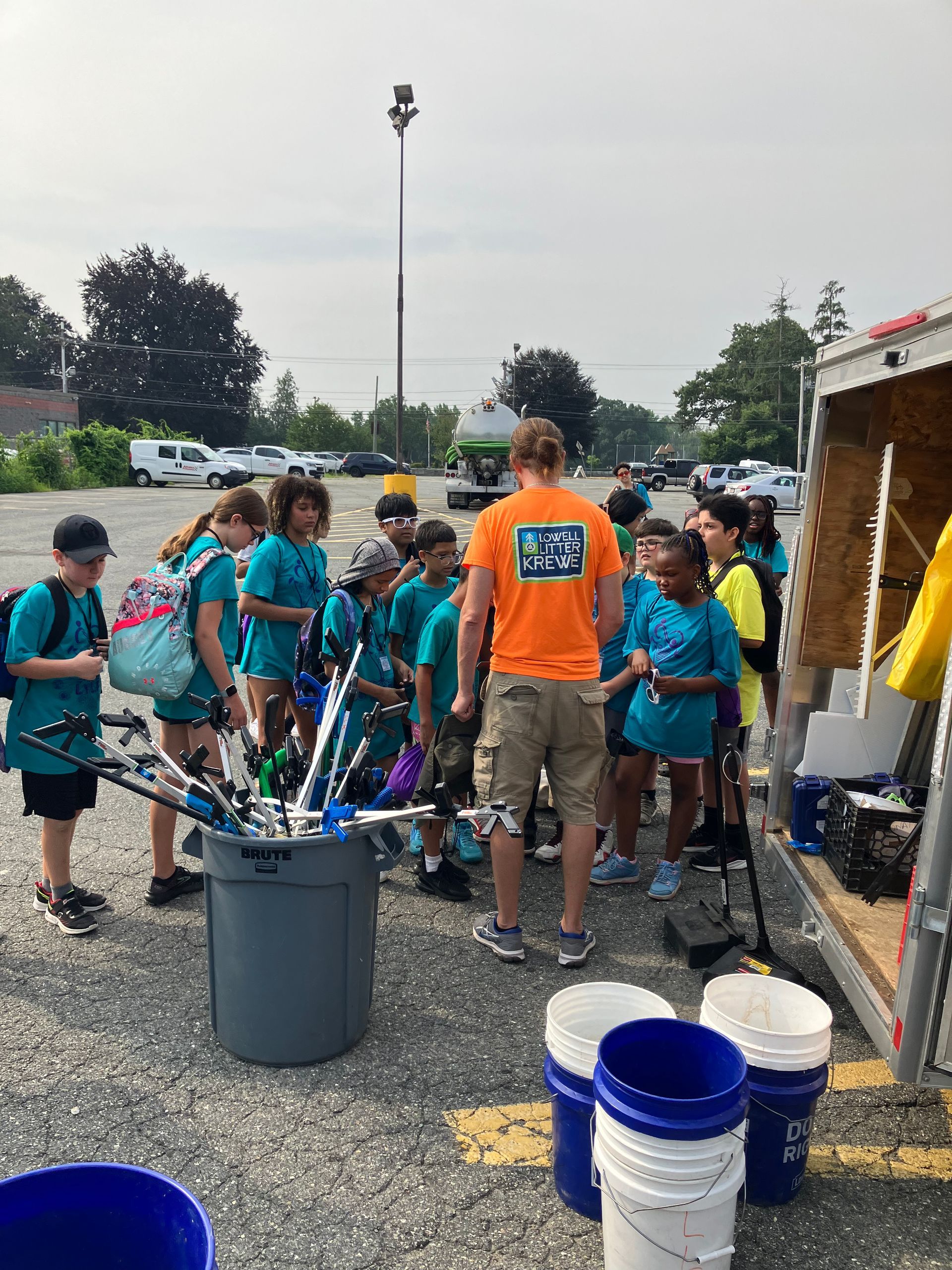 A group of children are standing around a bucket in a parking lot.