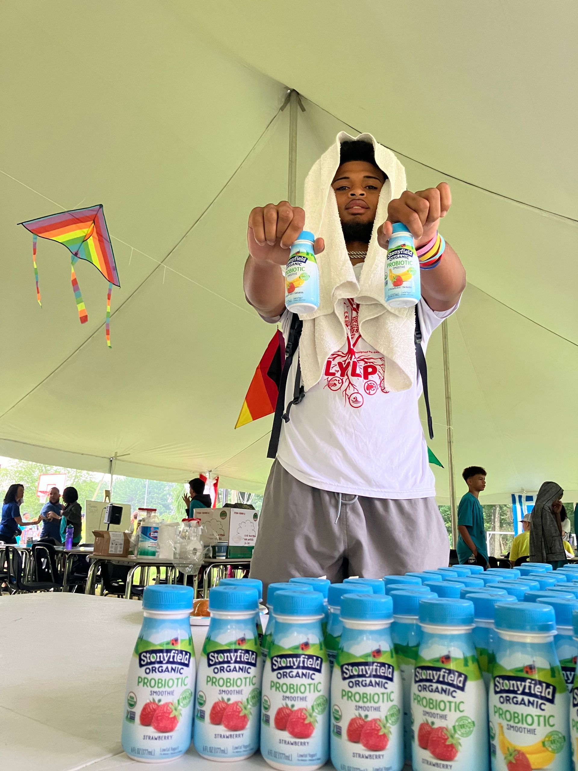 A man is standing under a tent holding bottles of yogurt.