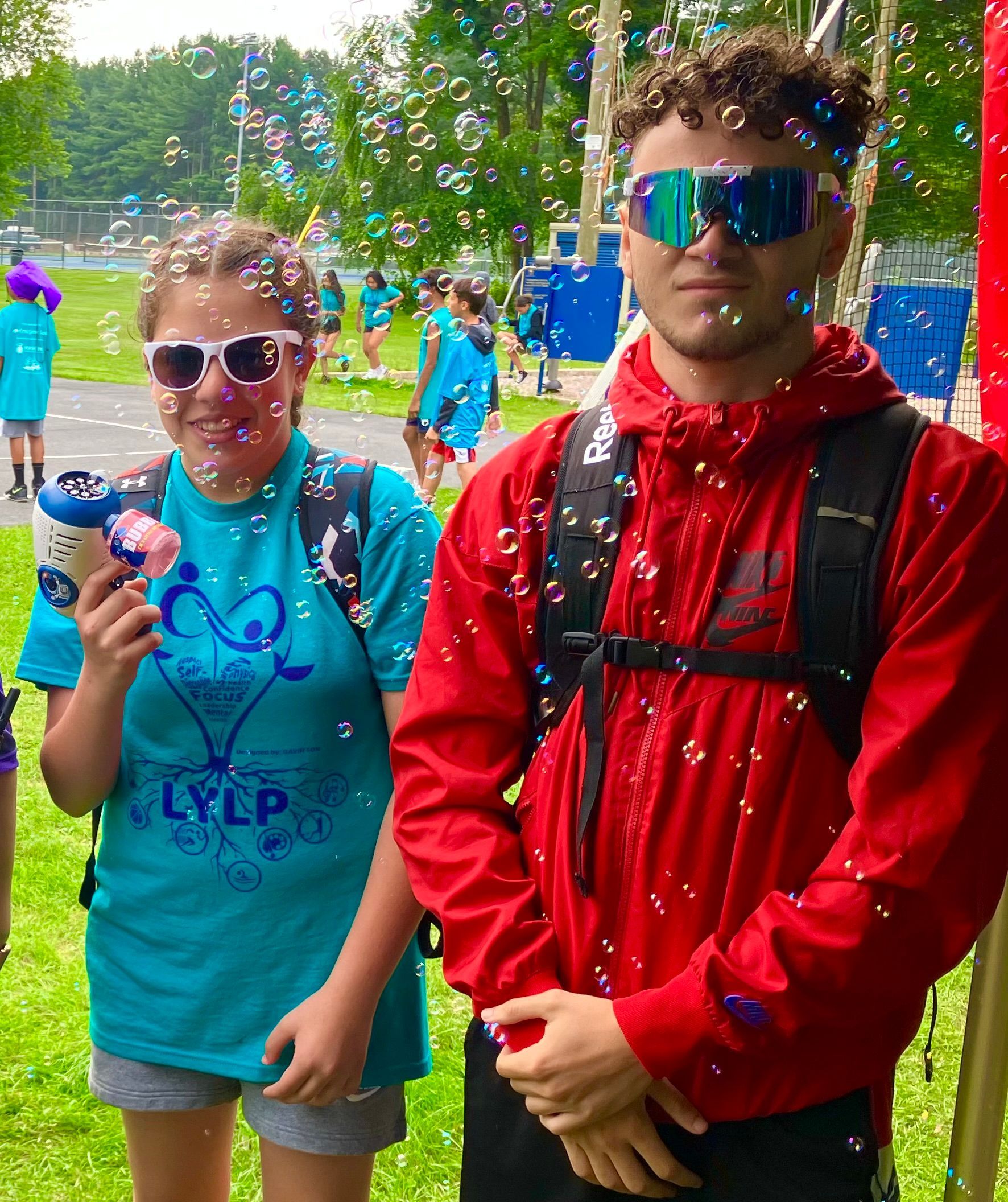 A man in a red jacket is standing next to a woman in a blue shirt that says lylp