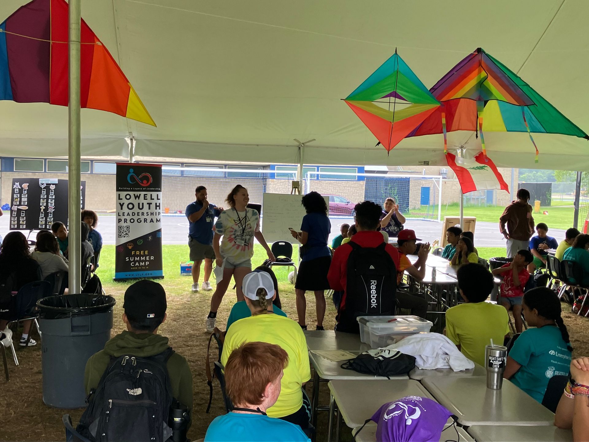 A group of people are sitting under a tent with kites hanging from the ceiling.