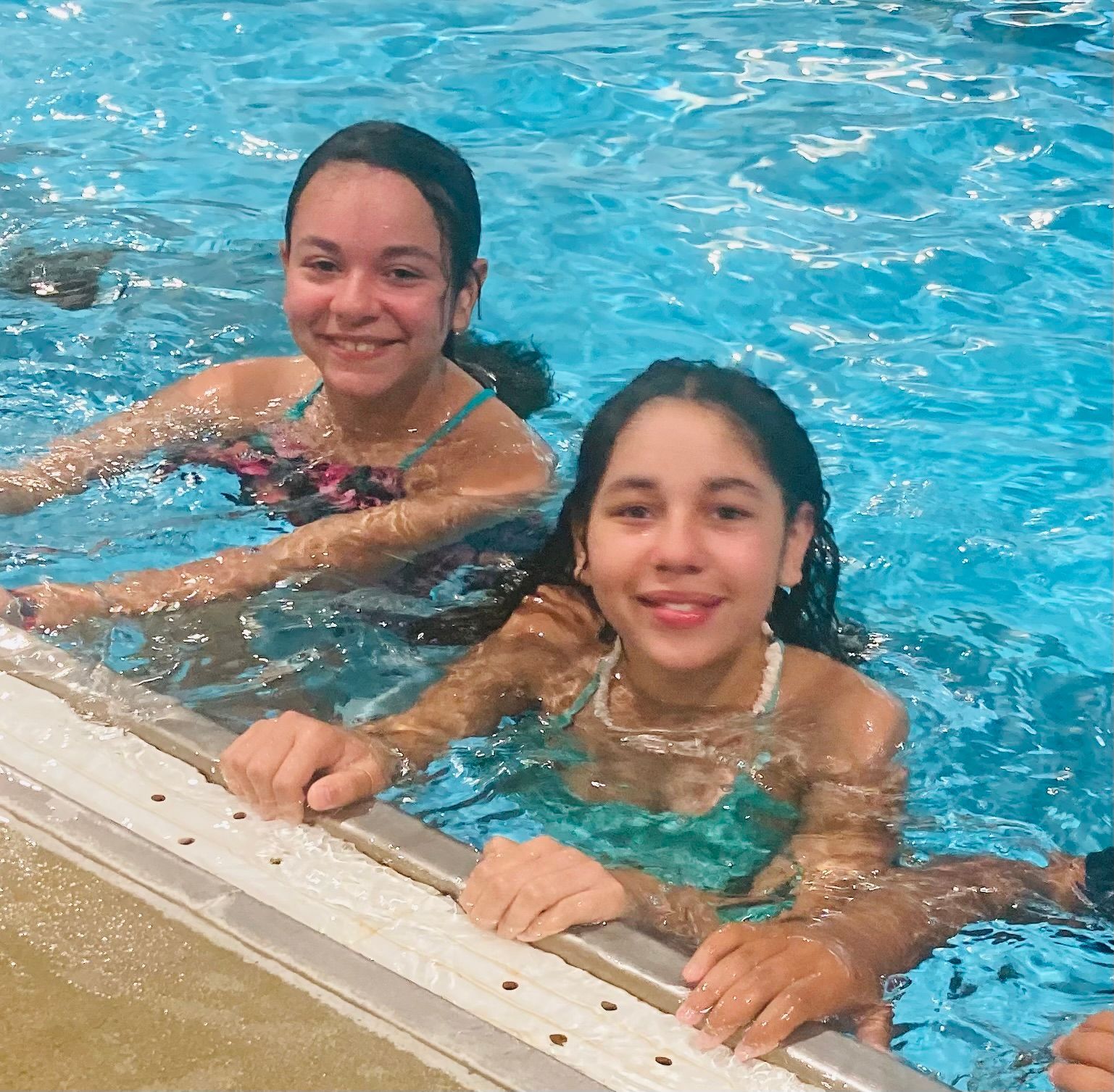 Two girls are swimming in a pool and smiling for the camera