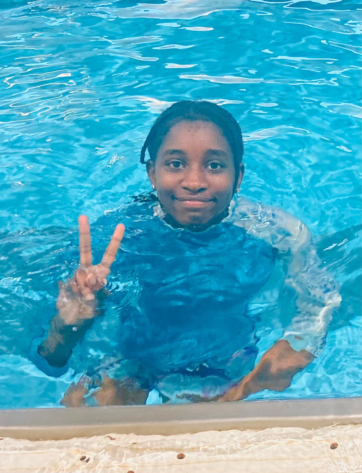 A young girl is swimming in a pool and giving a peace sign.