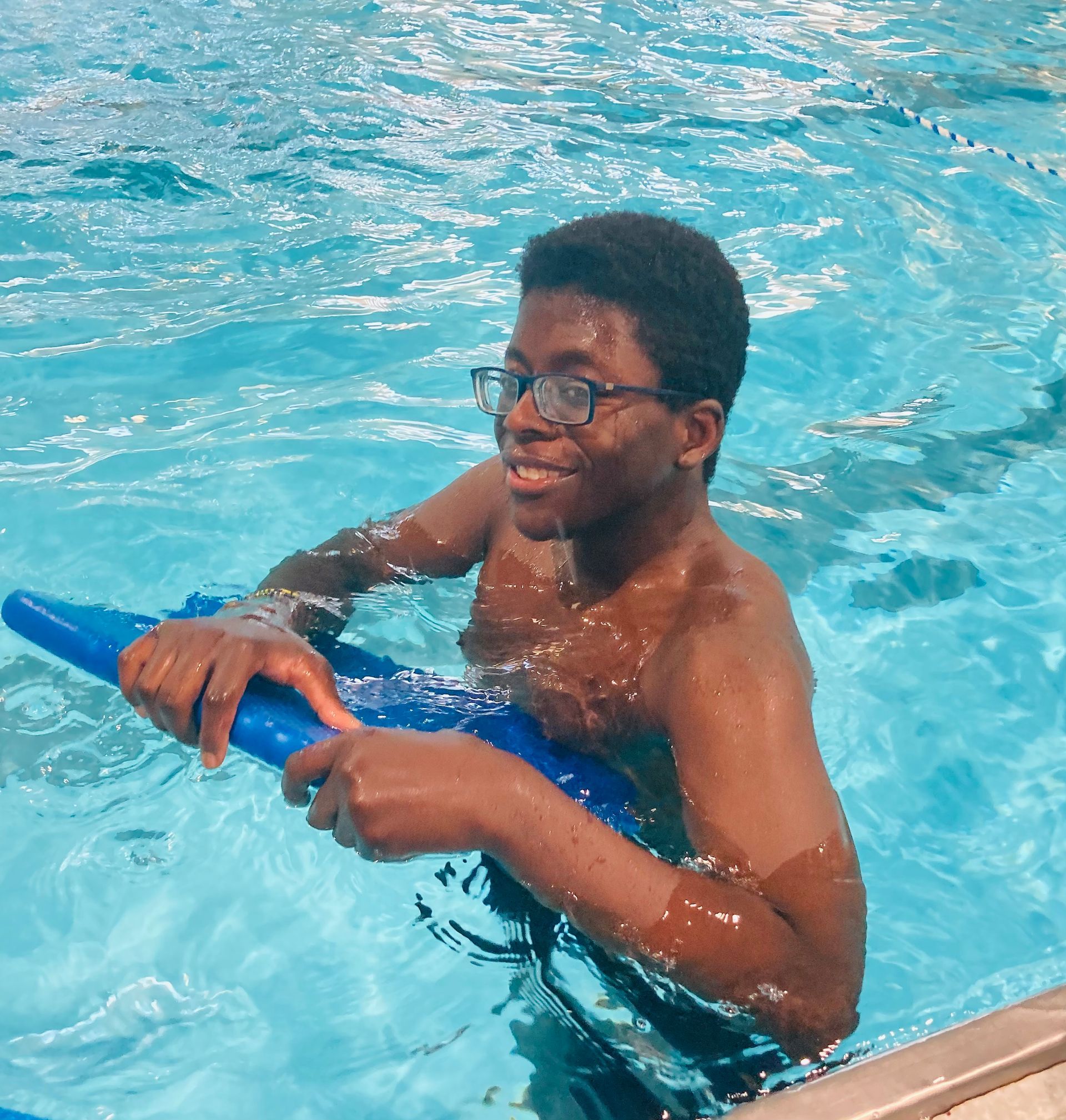 A man wearing glasses is holding a blue float in a swimming pool