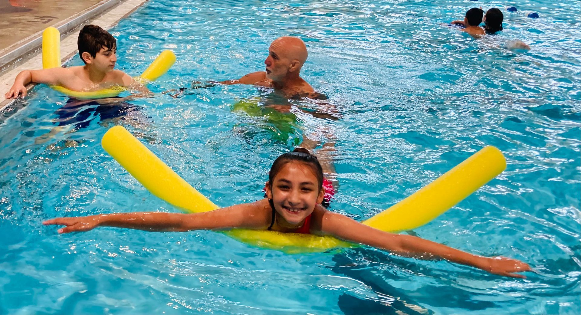 A girl is floating on a yellow noodle in a swimming pool.