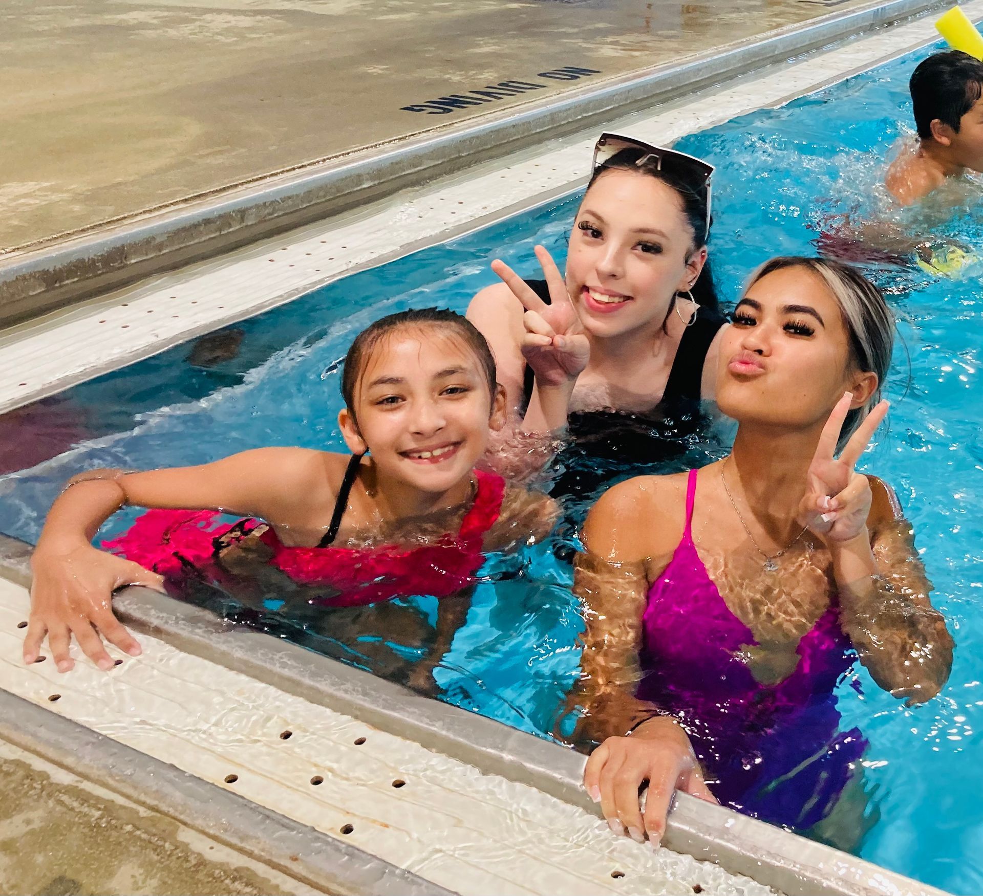 Three women are posing for a picture in a swimming pool