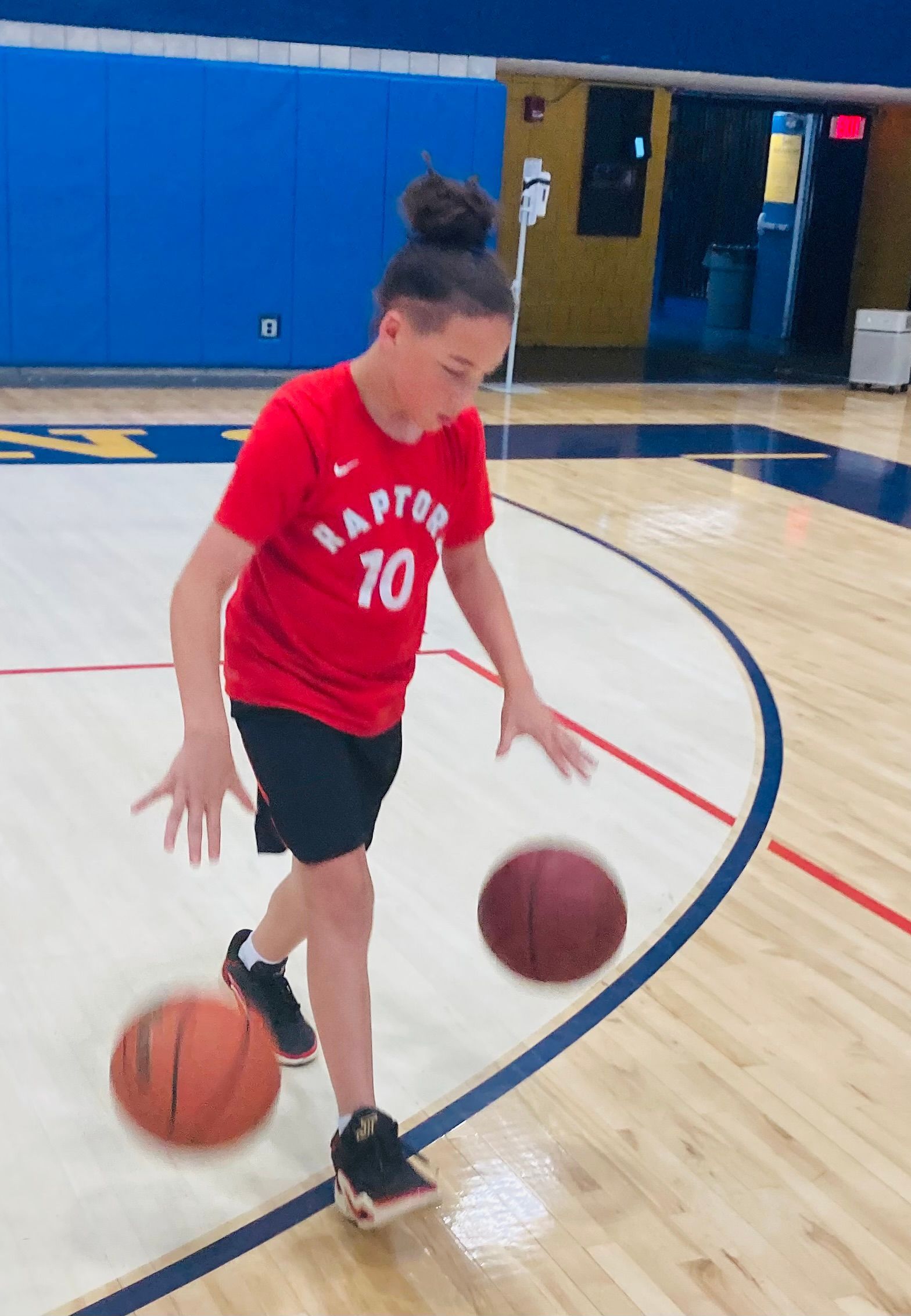 A girl wearing a red shirt with the number 10 on it is dribbling a basketball