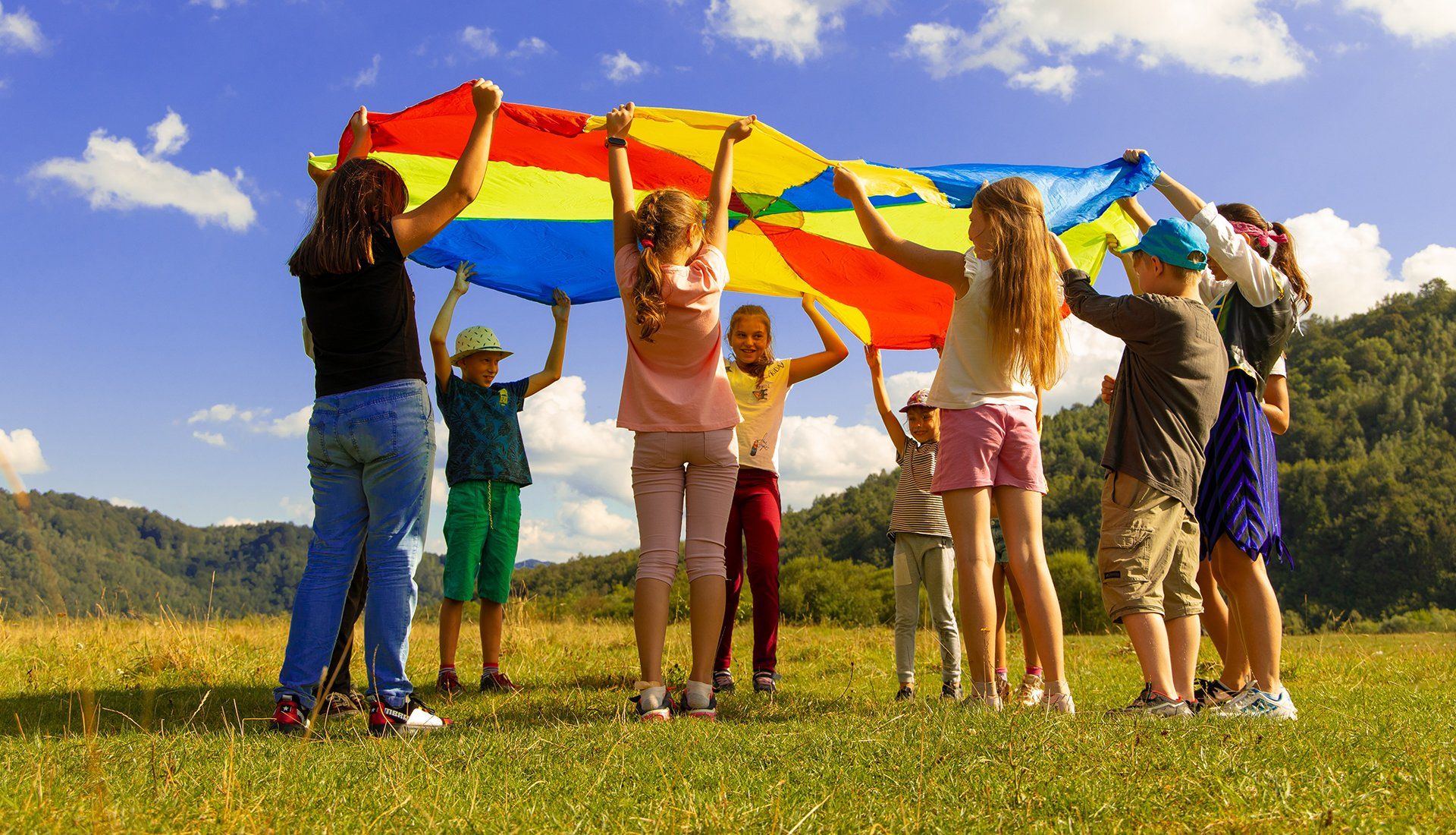 A group of children are holding a colorful parachute in a field.