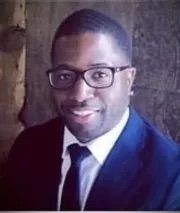 A man wearing glasses and a suit and tie is smiling for the camera.