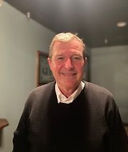 A man in a black sweater and white shirt is smiling for the camera.