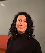 A woman with curly hair is wearing a black sweater and smiling for the camera.