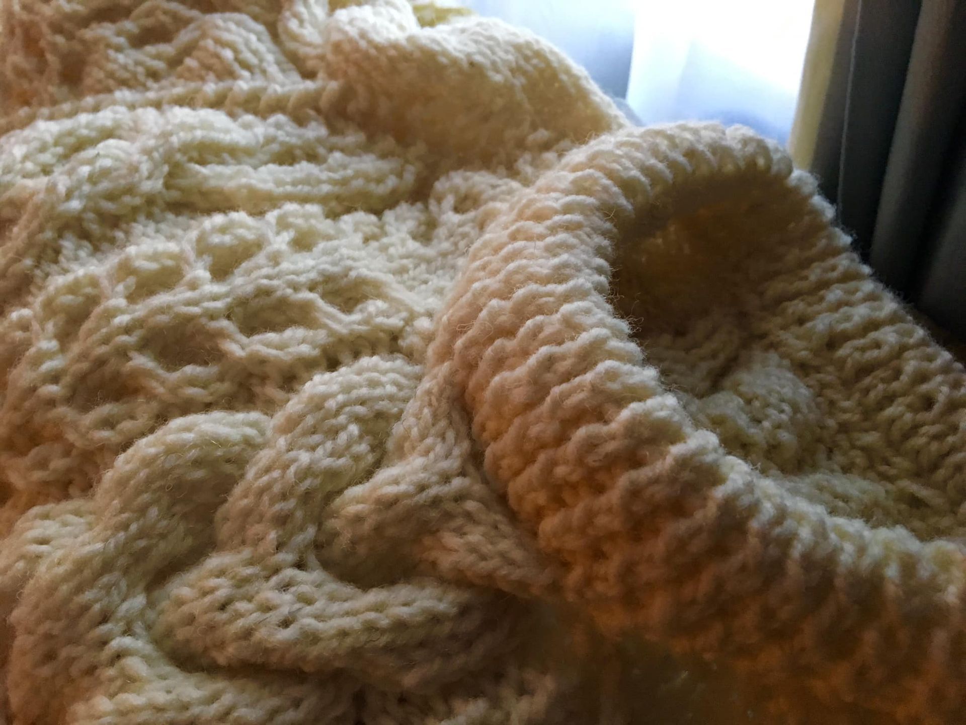 A close up of a white knitted blanket on a bed.