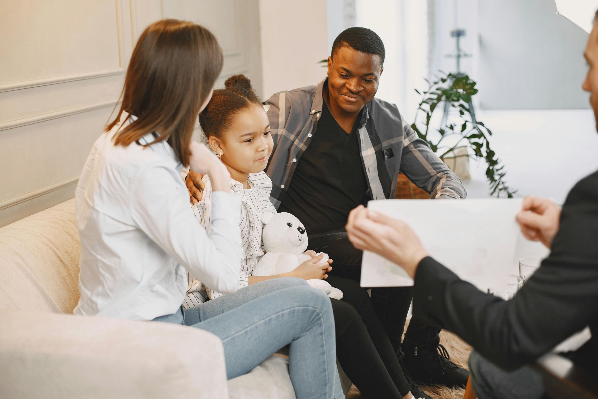 A professional counselor shows documents to a family sitting on a couch in a bright, modern office.