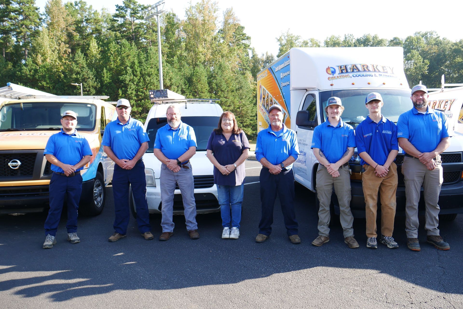 Group of service workers in blue shirts standing in front of vans.