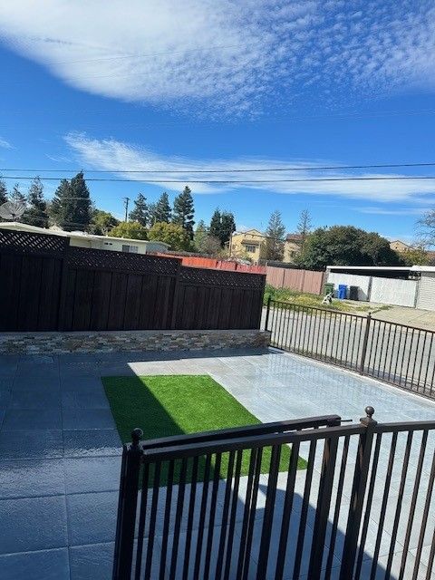 Backyard with brown fence, gray patio, green turf, black railing, and blue sky.