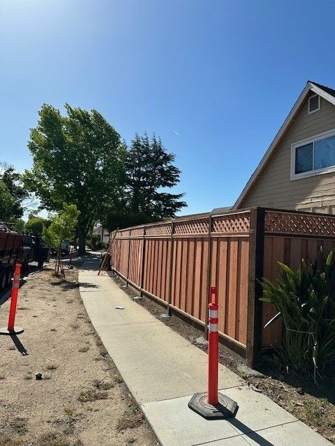 Wooden fence along a sidewalk next to a tan house under a blue sky.