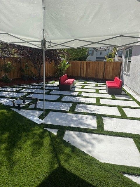 Patio with red chairs, stepping stones, and artificial turf under a white canopy.