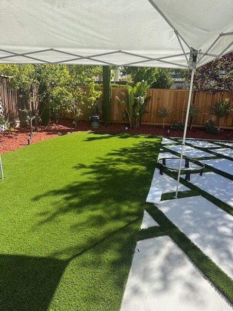 Backyard with green artificial grass, concrete pavers, a canopy, and landscaping.