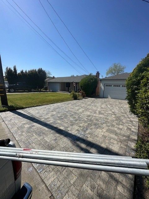 Driveway paved in gray blocks leads to a house on a sunny day; power lines overhead.