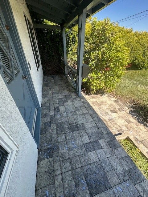 Blue-tiled porch with a door to the left. Overhang with railing on right, next to bushes and grass.