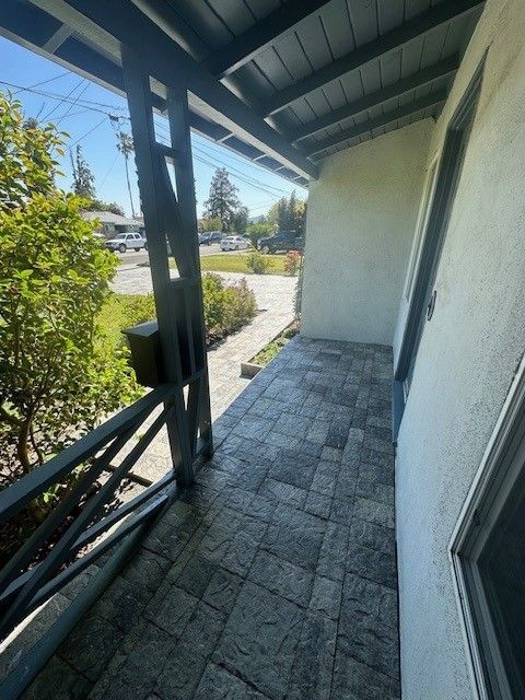 Covered porch with gray brick pavers, blue trim, and a view of a street.