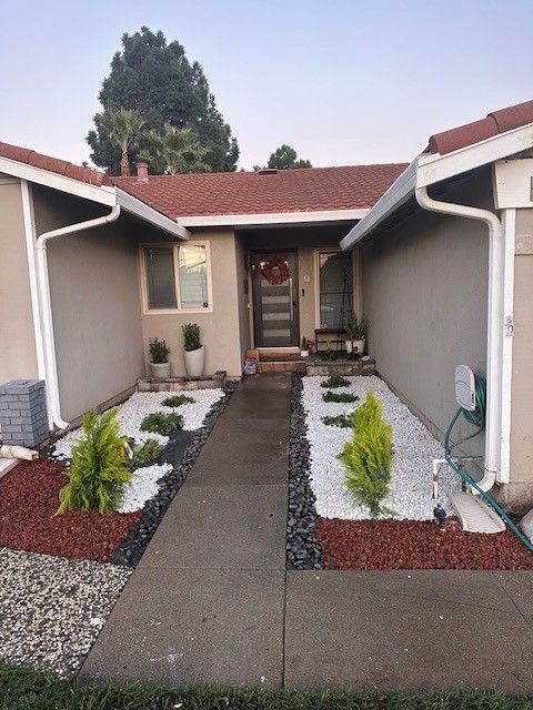 Beige house with red tile roof, path leading to front door. Landscaping features white and black stones with plants.