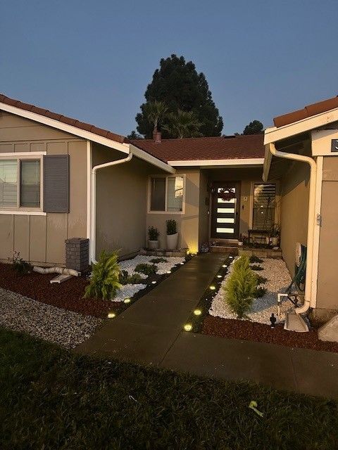 Tan house exterior with a pathway lit by ground lights, leading to the front door.