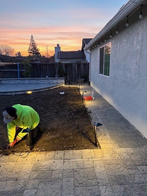 A person installing landscape lighting in a backyard at dusk.