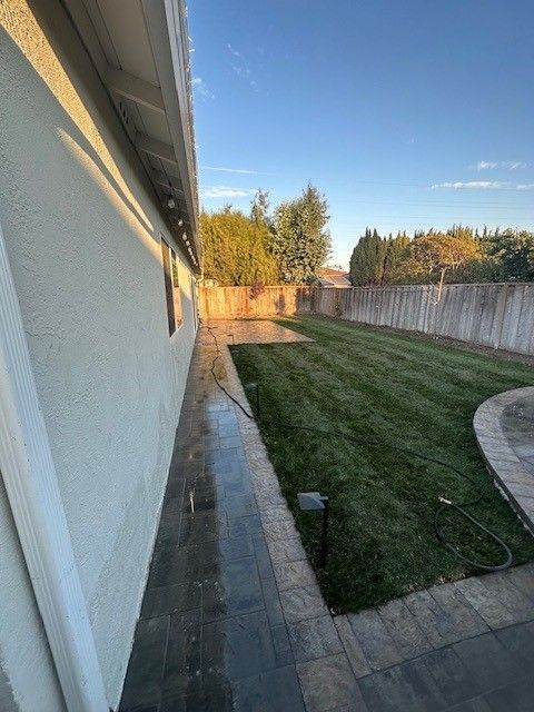 Backyard with green grass, stone patio, wooden fence, and house wall.