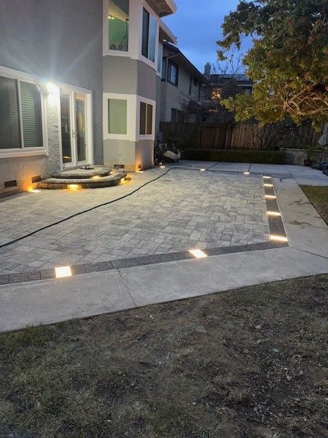 Backyard patio with paving stones and recessed lights at dusk. House in the background.