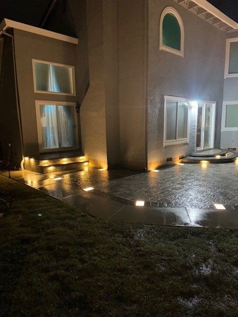 Night view of a house with outdoor lights illuminating the concrete patio and lawn.