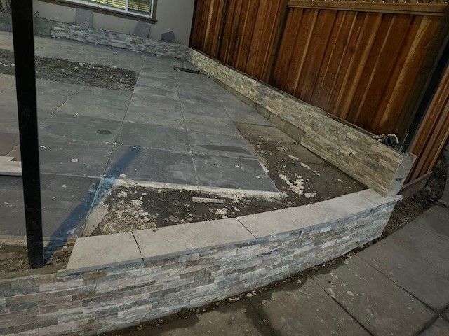 Stone patio under construction next to a wooden fence, with stacked stone edging.