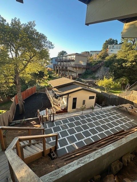 View of a home with steps, patio, and surrounding homes on a hillside on a sunny day.