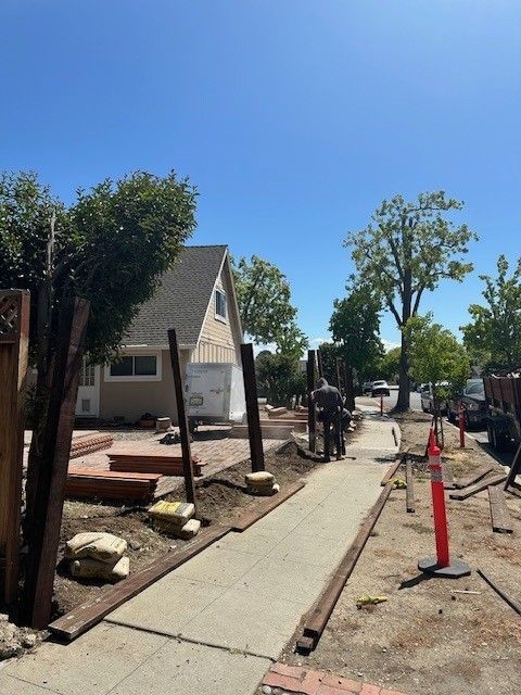 Workers building a fence next to a sidewalk in front of a house on a sunny day.