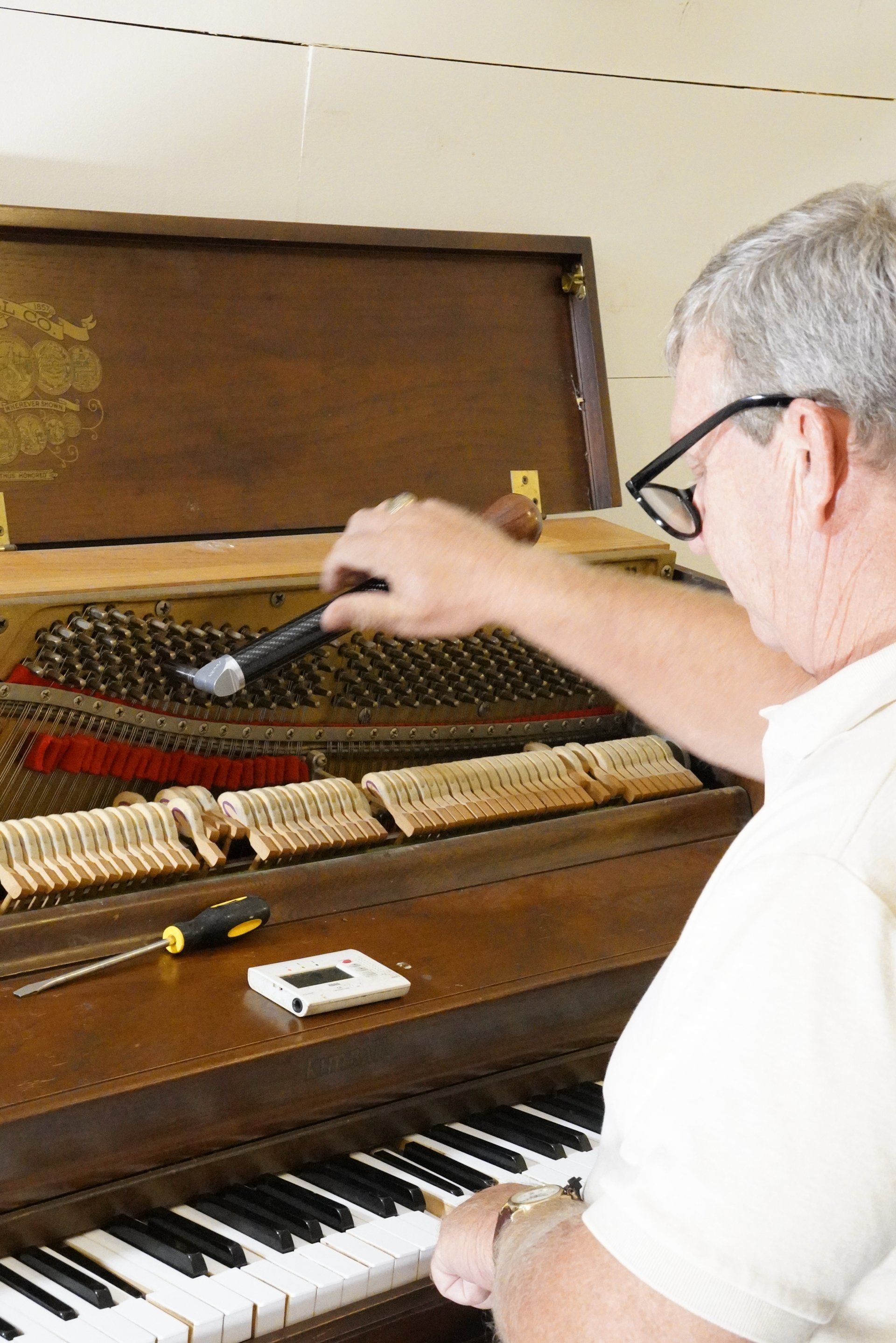 A man is working on a piano with a screwdriver